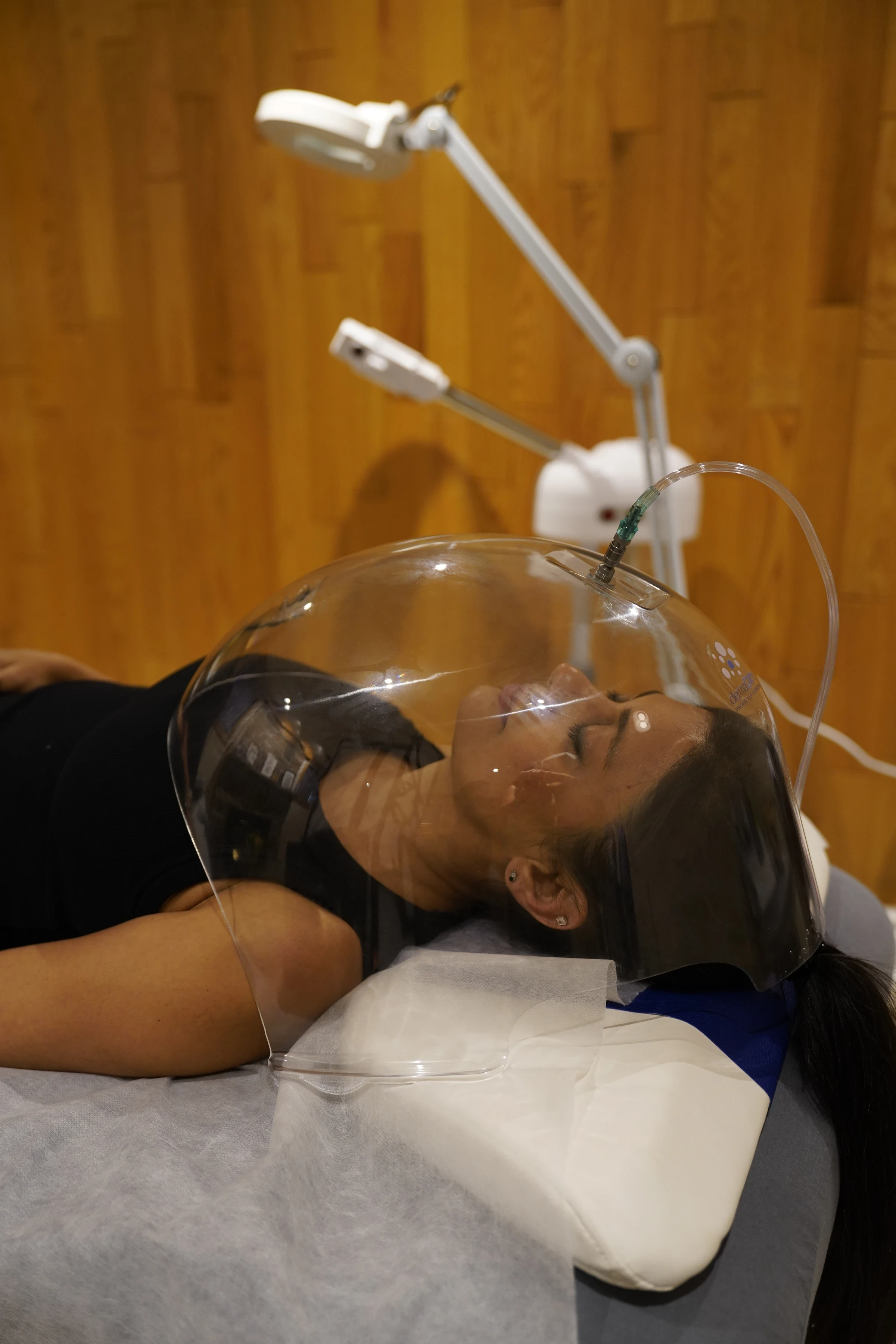 Client relaxing under the transparent oxygen dome during a facial treatment